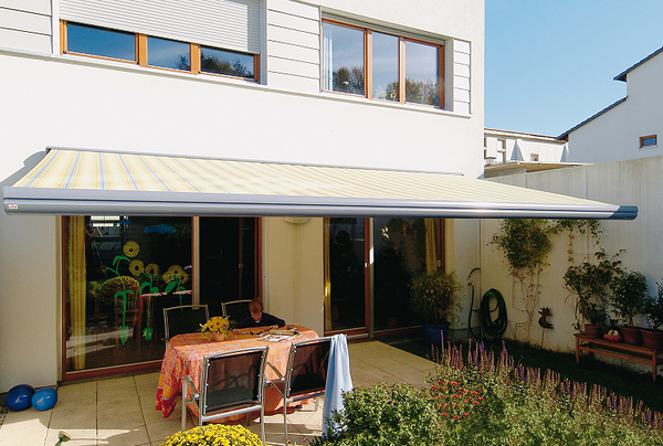 Eine gelb-gestreifte Markise spendet Schatten auf einer modernen Terrasse mit Garten.