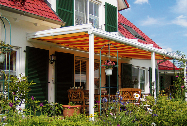 Terrassenüberdachung mit Markise an Einfamilienhaus, Gartenmöbel und Blumen im Vordergrund.