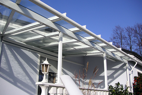 Moderne Terrassenüberdachung aus Glas an einem Einfamilienhaus mit Garten und Geländer.